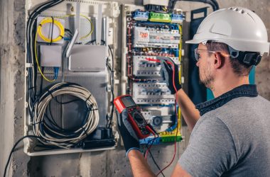 Man, an electrical technician working in a switchboard with fuses. Man, an electrical technician working in a switchboard with fuses. Installation and connection of electrical equipment. Professional uses a tablet.